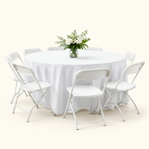 Round table with white linens, folding chairs and a floral centerpiece