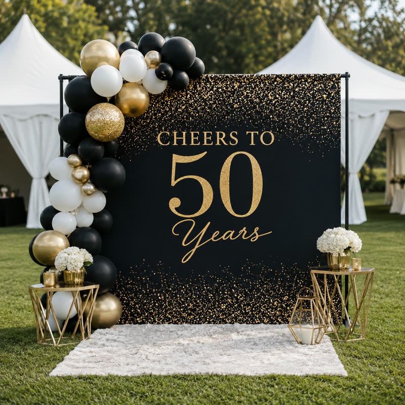 Black and gold celebration backdrop with balloon garland and accent tables